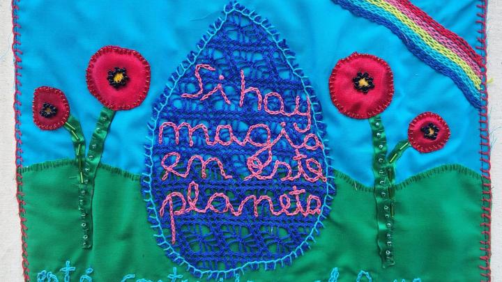 Pancarta textil sostenida en una estructura de madera, compuesta por múltiples bordados de colores que representan paisajes y escenas vinculadas al agua. En el centro se lee el mensaje “Nuestros cauces, nuestra causa”.